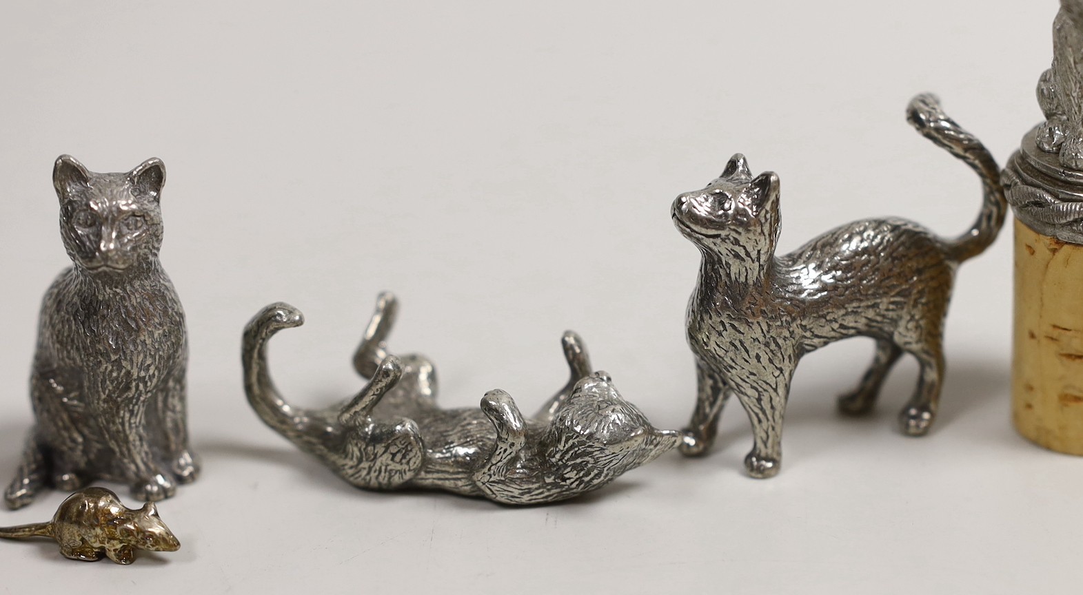 A modern silver miniature free standing model of a cat, with raised paw, London, 1995, length 37mm, together with four other base metal cats and a mouse and a cork stopper with cat finial.